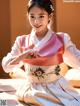 A woman in a pink and white hanbok sitting on a bed.