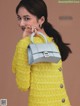 A woman in a yellow sweater holding a silver handbag.