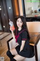 A woman in a school uniform sitting on a couch holding a drink.