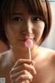 A woman holding a pink lollipop in her mouth.