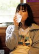 A woman sitting on a bench drinking water from a glass.