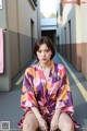 A woman in a purple and orange kimono sitting on the ground.