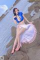 A woman in a blue bikini sitting on a rock by the water.